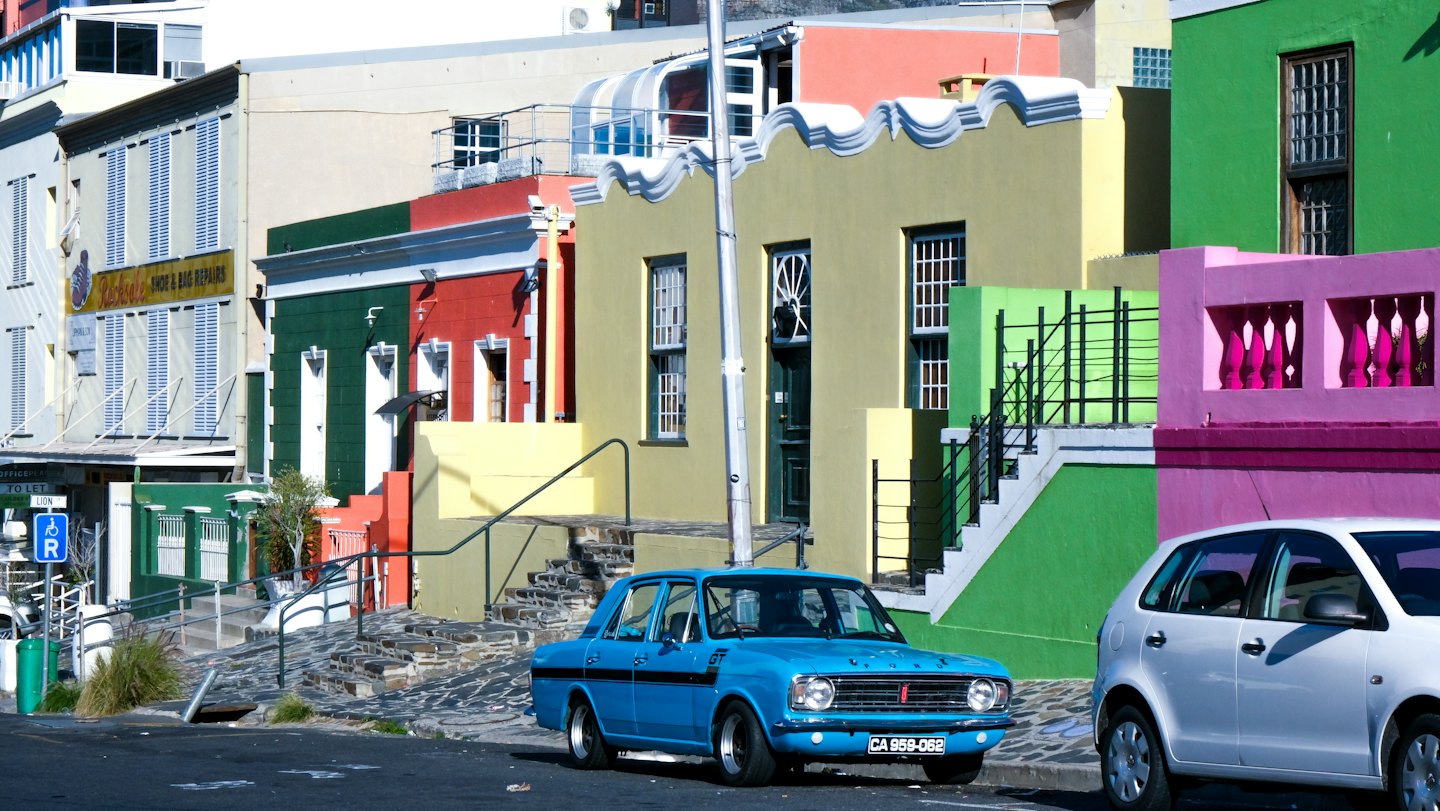 Colorful houses and parked cars line a city street.