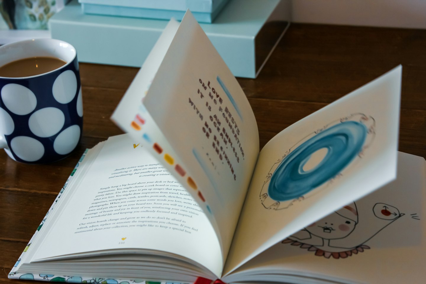 Open illustrated book and a polka dot mug on a table.