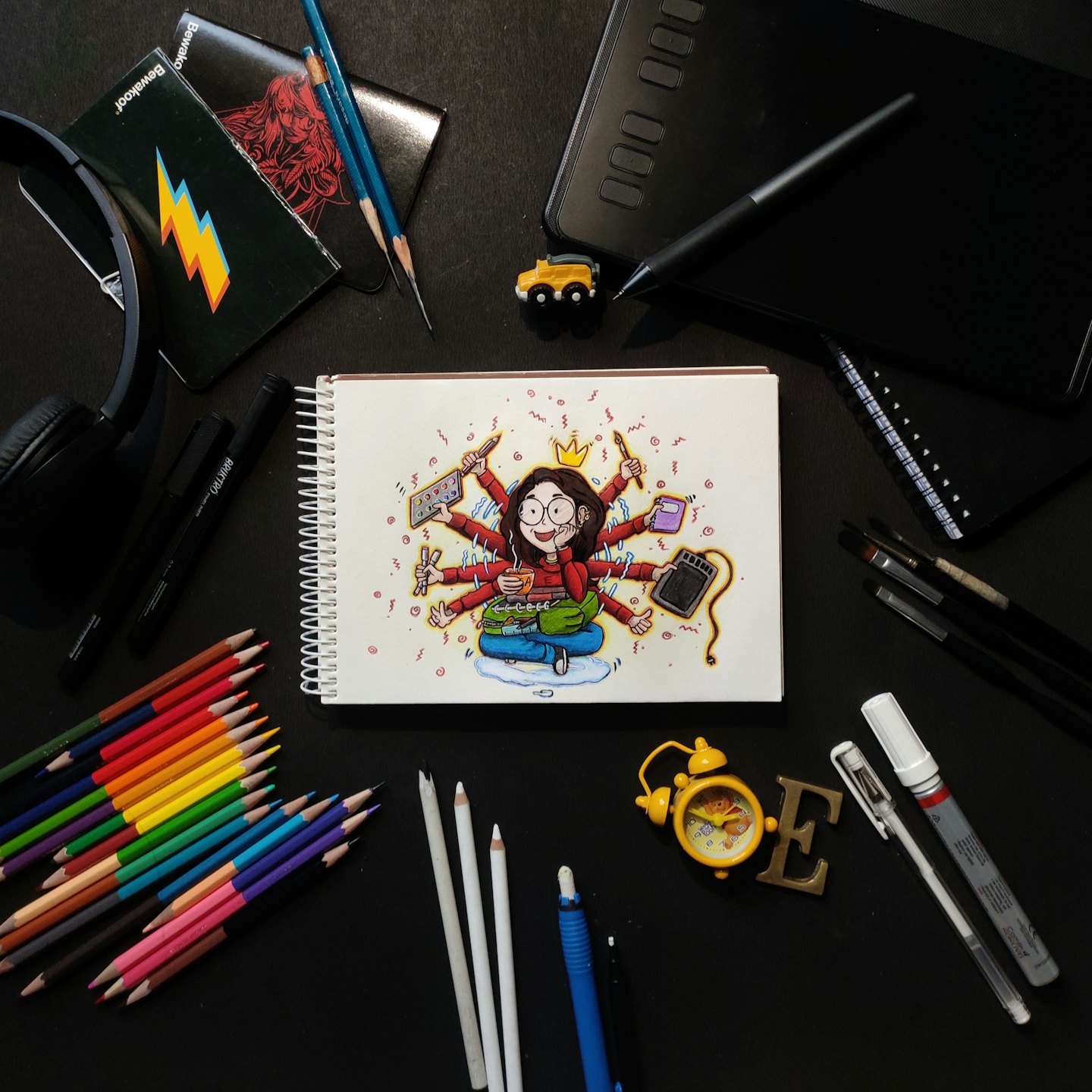 Art supplies and a sketchbook featuring a multitasking woman illustration.