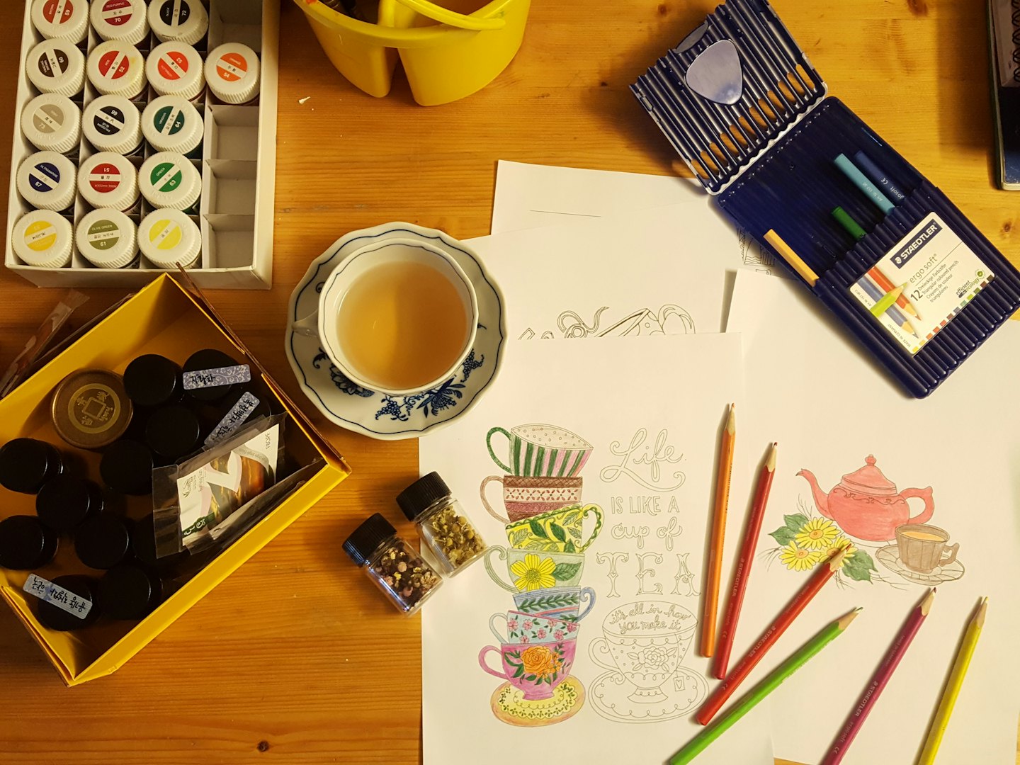 Art supplies and a teacup on a wooden table.